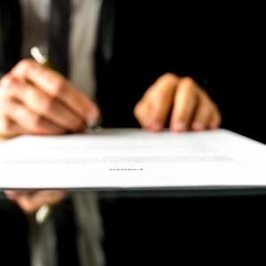 Close up low angle view of the blurred hands of a businessman signing a document or contract with focus to the text Contract. Shallow dof.