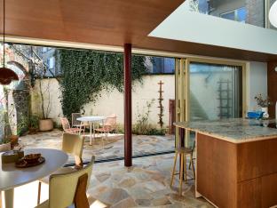 De blikvanger van de woning: voorheen een labo, nu een lichtrijke keuken plus eetruimte met vide. De mozaïek van terrastegels loopt naar binnen, waardoor het stadskoertje onderdeel wordt van het interieur.