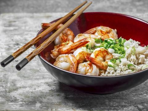 A bowl of rice, shrimp and chopped scallion on a wooden cutting board