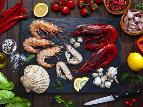 Top view of a black slate table with mollusks and crustacean ready for cooking on a wood kitchen counter top. Ingredients for cooking like olive oil, salt and pepper, garlic, lemon and herbs are all around the frame. DSRL studio photo taken with Canon EOS 5D Mk II and Canon EF 70-200mm f/2.8L IS II USM Telephoto Zoom Lens