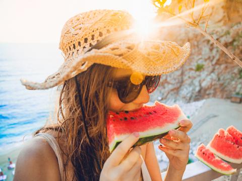 young woman having fun and eating juicy fresh watermelon outdoor at sunset time with sunflare in summer time