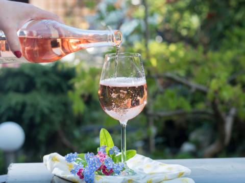 Waiter pouring a glas of cold rose wine, outdoor terrase, sunny day, green garden background