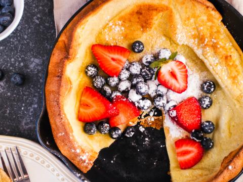 Dutch Baby Pancakes with berries and powdered sugar baked in oven on iron pan, top view