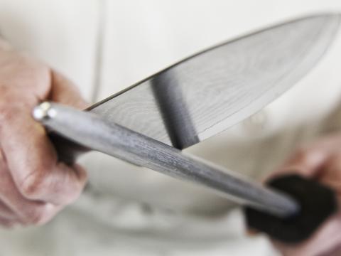 Close-up of a chef sharpening a large kitchen knife blade with a steel.