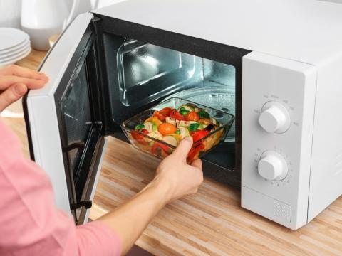 Woman putting bowl with vegetables in microwave oven, closeup