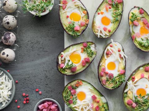 Keto diet dish: Avocado boats with ham cubes, quail eggs, cheese and cress sprouts on stone serving board