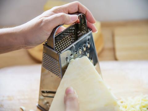 Woman preparing cheese for cook using cheese grater in the kitchen - people making food with cheese concept