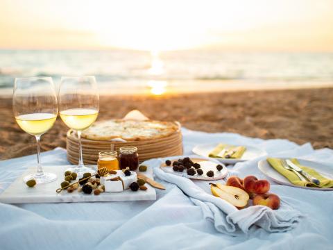 Beautiful served picnic at seaside on sunset. Romantic picnic for two with fruits, snacks, white wine and cheese pizza on a linen blanket. Idea for weekend.