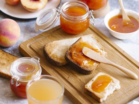 Toasts of bread with apricot jam and fresh fruits with leaves on white wooden table. Tasty breakfast.