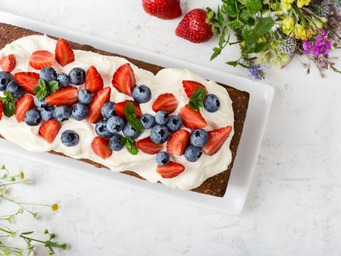 Summer baking with strawberries and blueberries.  Cake loaf with buttercream icing and topped with fresh ripe summer colorful fruits and berries, top view, selective focus
