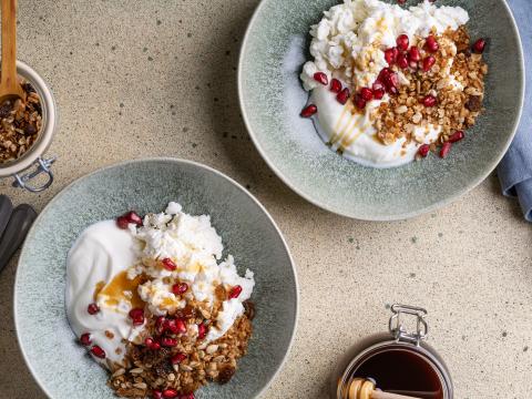 Healthy breakfast, homemade granola with cottage cheese, kefir, pomegranate, and honey in bowl, trending foods, fermented foods, high angle view