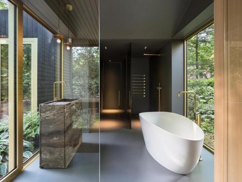 Een donkere vloer, plafond en douchewand creëren een intieme setting voor een badkamer met subtiele grandeur. De doorlopende ramen omkaderen de natuur.© Giulia Frigerio