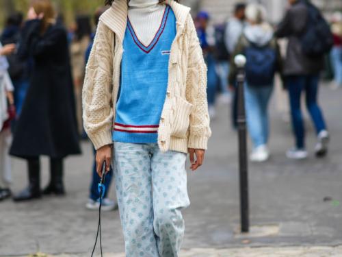 PARIS, FRANCE - OCTOBER 01: A guest wears a white ribbed turtleneck long sleeves t-shirt, a blue wool with red stripes on the collar / V-neck / oversized pullover, a white latte braided wool zipper cardigan, pale blue with blue print flower pattern denim large ripped pants, black and white striped socks, white leather sneakers, outside Loewe, during Paris Fashion Week - Womenswear Spring Summer 2022, on October 01, 2021 in Paris, France. (Photo by Edward Berthelot/Getty Images)