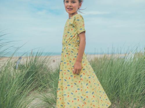 VakantiemoodZachtgele jurk (42,95 euro) met prints van de zon, een parasol en een ijsje: het feest kan niet meer stuk, van Baba Kidswear.