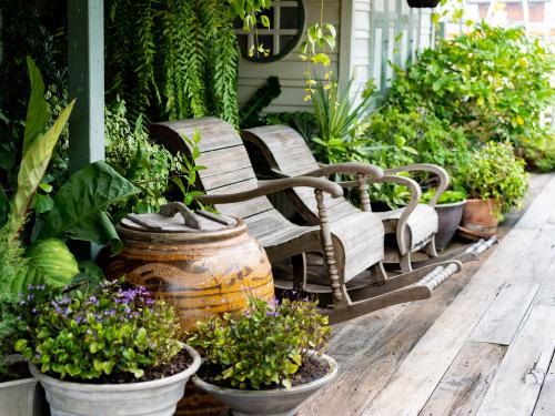 Wooden rocking chairs in a cottage garden porch setting on wooden floor in vintage Thai botanical garden, with traditional Thai old water jar decoration.