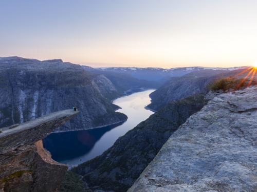 Sunset on the Norwegian fjord Trolltunga. Couple hiker sitting on a cliff above a lake, Trolltunga, Norway Concept of adventure, freedom and extreme lifestyle