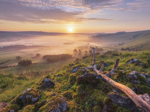 Hope valley on a beautiful misty morning in September 2020 with gritstone rocks and old tree branch in the foreground, Taken at sunrise in the Derbyshire Peak District National park. Castleton, Hope Valley, UK.