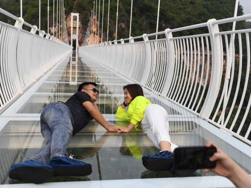 A couple pose for photos on the Bach Long glass bridge in Moc Chau district in Vietnam's Son La province on April 29, 2022. - Vietnam launched a new attraction for tourists -- with a head for heights -- on April 29 with the opening of a glass-bottomed bridge suspended some 150 metres above a lush, jungle-clad gorge. (Photo by Nhac NGUYEN / AFP)