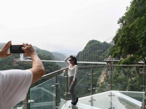 A visitor poses for photos on the walkway section of the Bach Long glass bridge in Moc Chau district in Vietnam's Son La province on April 29, 2022. - Vietnam launched a new attraction for tourists -- with a head for heights -- on April 29 with the opening of a glass-bottomed bridge suspended some 150 metres above a lush, jungle-clad gorge. (Photo by Nhac NGUYEN / AFP)