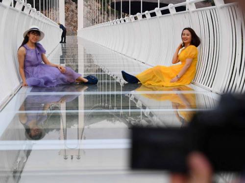 This photo taken on April 28, 2022 shows visitors posing for photos on the Bach Long glass bridge in Moc Chau district in Vietnam's Son La province. - Vietnam launched a new attraction for tourists -- with a head for heights -- on April 29 with the opening of a glass-bottomed bridge suspended some 150 metres above a lush, jungle-clad gorge. (Photo by Nhac NGUYEN / AFP)