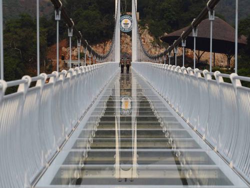 This photo taken on April 28, 2022 shows security guards walking on the Bach Long glass bridge in Moc Chau district in Vietnam's Son La province. - Vietnam launched a new attraction for tourists -- with a head for heights -- on April 29 with the opening of a glass-bottomed bridge suspended some 150 metres above a lush, jungle-clad gorge. (Photo by Nhac NGUYEN / AFP)