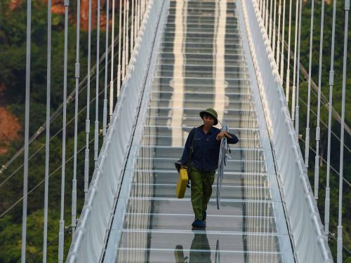 This photo taken on April 28, 2022 shows a worker walking on the Bach Long glass bridge in Moc Chau district in Vietnam's Son La province. - Vietnam launched a new attraction for tourists -- with a head for heights -- on April 29 with the opening of a glass-bottomed bridge suspended some 150 metres above a lush, jungle-clad gorge. (Photo by Nhac NGUYEN / AFP)