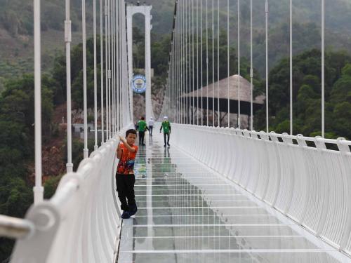 A young visitor makes his way across the Bach Long glass bridge in Moc Chau district in Vietnam's Son La province on April 29, 2022. - Vietnam launched a new attraction for tourists -- with a head for heights -- on April 29 with the opening of a glass-bottomed bridge suspended some 150 metres above a lush, jungle-clad gorge. (Photo by Nhac NGUYEN / AFP)