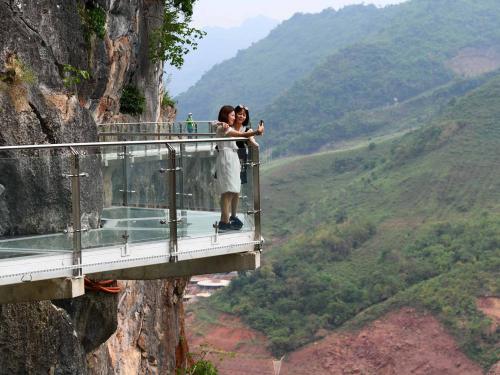 Visitors take photos on the walkway section of the Bach Long glass bridge in Moc Chau district in Vietnam's Son La province on April 29, 2022. - Vietnam launched a new attraction for tourists -- with a head for heights -- on April 29 with the opening of a glass-bottomed bridge suspended some 150 metres above a lush, jungle-clad gorge. (Photo by Nhac NGUYEN / AFP)