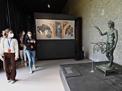 Visitors look at a sculpture of Ephebe lamp-holder, in Pompeii's site during a new exhibition entitled "Art and sensuality in the houses of Pompeii" on art and sexuality in the ancient city, where sculptures and paintings of breasts and buttocks abounded, on April 28, 2022. - Raunchy scenes may redden faces at a new exhibition in Pompeii on art and sexuality in the ancient Roman city, where sculptures and paintings of breasts and buttocks abounded. Archaeologists excavating the city, which was destroyed by the eruption of nearby Vesuvius in 79 AD, were initially startled to discover erotic images everywhere, from garden statues to ceiling frescos. (Photo by Andreas SOLARO / AFP)