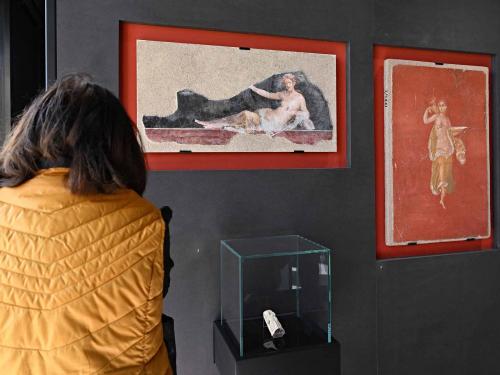 A visitor looks on during a new exhibition in Pompeii's site entitled "Art and sensuality in the houses of Pompeii" on art and sexuality in the ancient city, where sculptures and paintings of breasts and buttocks abounded, on April 28, 2022. - Raunchy scenes may redden faces at a new exhibition in Pompeii on art and sexuality in the ancient Roman city, where sculptures and paintings of breasts and buttocks abounded. Archaeologists excavating the city, which was destroyed by the eruption of nearby Vesuvius in 79 AD, were initially startled to discover erotic images everywhere, from garden statues to ceiling frescos. (Photo by Andreas SOLARO / AFP)