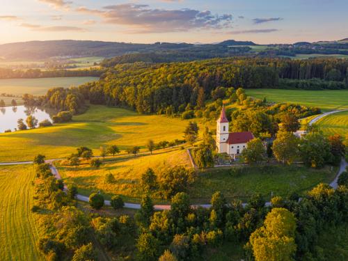 Church on the hill with sunlit summer landscape from above. Bysicky church near SPA town Lazne Belohrad, Czech Republic. Sunset gold light.
