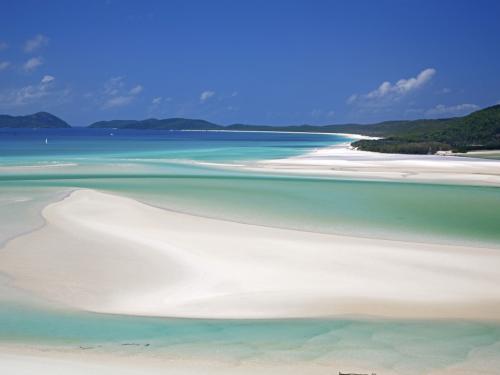 The pure white sand and cool aqua blue waters of Whitehaven Beach where the forest meets the sea in the Whitsunday Islands. Sailing boats and islands in the distance. Horizontal, copy space.