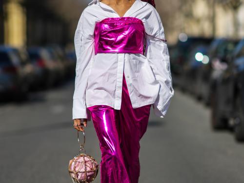 PARIS, FRANCE - MARCH 08: Debbie @blackhey wears a gold flower pattern headband, gold large earrings from Givenchy, orange sunglasses, a white oversized shirt, a neon pink shiny leather shoulder-off / cropped top, matching neon pink shiny leather large pants, a gold chain circle handbag with a pale purple clutch inside, white leather sneakers, outside Chanel, during Paris Fashion Week - Womenswear F/W 2022-2023, on March 08, 2022 in Paris, France. (Photo by Edward Berthelot/Getty Images)