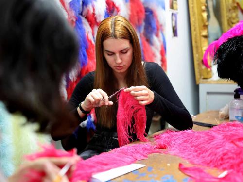 An assistant of Dominique De Roo, official feather craftsman of the Lido cabaret, works on a feather costume inside the workshop, in Paris, on June 1, 2022. - The Lido cabaret, an institution for Parisian night life since 1889, is set to lay off 157 of 184 employees, including its "Bluebell girls" troupe of dancers, announced the new owner, French hotels giant Accor. (Photo by Thomas COEX / AFP)