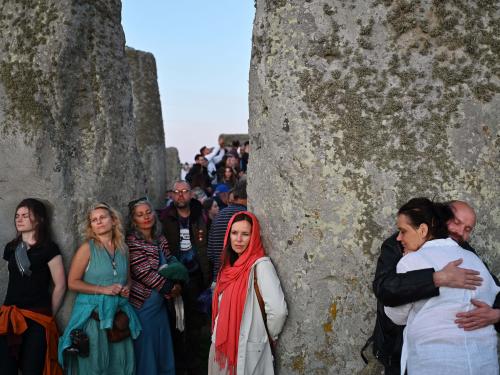Revelers interact with the stone monument as the sun sets behind the stones at Stonehenge, near Amesbury, in Wiltshire, southern England on June 20, 2022, on the eve of a festival, dating back thousands of years, that will celebrate the longest day of the year when the sun will be at its maximum elevation. - The stone monument -- carved and constructed at a time when there were no metal tools -- symbolises Britain's semi-mythical pre-historic period, and has spawned countless legends. (Photo by Justin TALLIS / AFP)