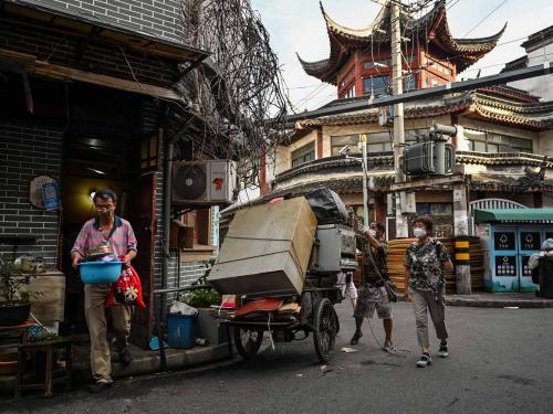 This photo taken on July 3, 2022 shows a collector, who buys antique furniture and other household items from relocating residents, stacking items on a cart as people walk past in the Laoximen neighbourhood of Shanghai's Huangpu district. - Bricked-up doorways, crumbling facades, and a small group of defiant locals: one of Shanghai's oldest neighbourhoods is barely clinging to life as the city presses ahead with demolition and redevelopment plans. (Photo by Hector RETAMAL / AFP)