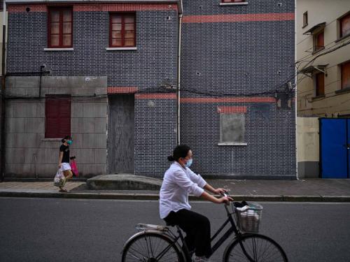 This photo taken on June 22, 2022 shows people cycling and walking past a sealed building marked for demolition in the Laoximen neighbourhood of Shanghai's Huangpu district. - Bricked-up doorways, crumbling facades, and a small group of defiant locals: one of Shanghai's oldest neighbourhoods is barely clinging to life as the city presses ahead with demolition and redevelopment plans. (Photo by Hector RETAMAL / AFP)