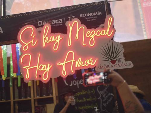 A neon signs reads "If There is Mezcal, There is Love" at a stand selling mezcal at the Mezcal Fair in Oaxaca, Mexico, on July 26, 2022. - Craft distillers fear mezcal will become victim of its own success. The fast-growing popularity of Tequila's lesser-known cousin is raising concerns about its sustainability as strong demand means that more land, water and firewood are needed to grow the agave plants and distill the smoky spirit. Faced with the boom, craft producers are committed to saving wild species by planting them and showcasing the artisanal process behind the liquor. (Photo by Pedro PARDO / AFP)
