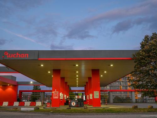 This photograph taken on August 29, 2022 in Budapest's 11th district, Hungary, shows a petrol station French multinational company Auchan, at dusk. - A vintage pump in the Vietnamese hills; a Madrid petrol station topped with a giant sombrero; a multi-coloured futuristic fuel outlet in Dubai  whatever its form the humble filling stop, emblem of our modern societies, would appear to be running out of road. (Photo by Attila KISBENEDEK / AFP)