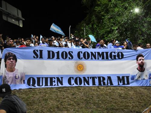 BUENOS AIRES, ARGENTINA - DECEMBER 20: Fans of Argentina display a flag of Lionel Messi and late football legend Diego Maradona before the arrival of the Argentina men's national football team after winning the FIFA World Cup Qatar 2022 on December 20, 2022 in Buenos Aires, Argentina. (Photo by Rodrigo Valle/Getty Images)