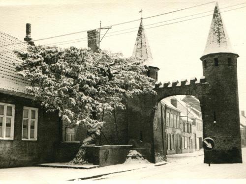 Een foto van de Westpoort te Lo tijdens de winter van 1958. De middeleeuwse poort uit het einde van de 14e eeuw is de enige overblijvende van de vier stadspoorten die Lo rijk was. De poort werd voor het eerst gerestaureerd in 1848.