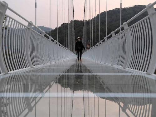 This photo taken on April 28, 2022 shows a staff member walking on the Bach Long glass bridge in Moc Chau district in Vietnam's Son La province. - Vietnam launched a new attraction for tourists -- with a head for heights -- on April 29 with the opening of a glass-bottomed bridge suspended some 150 metres above a lush, jungle-clad gorge. (Photo by Nhac NGUYEN / AFP)