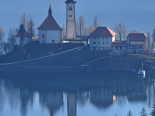 L’église Marie de l’Assomption sur l’ïle Blesjsky Ototkau centre du lac de Bled en Slovénie, zoomée quelque 90x et améliorée par l’IA.