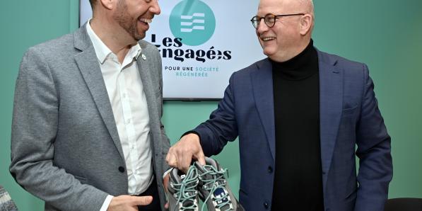 Maxime Prévot offrant des chaussures de marche (aux lacets turquoise) en guise de cadeau de bienvenue au randonneur Jean-Luc Crucke.