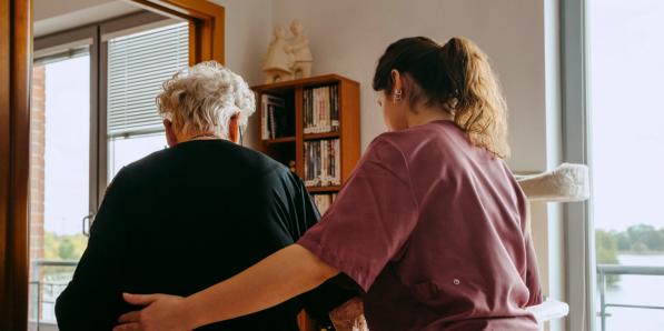 Een foto van een woonzorgcentrum waarop een oudere wordt begeleid door een medewerker.