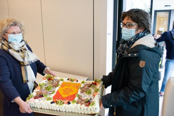 Katrien De Vlieger en Helle Lust, de voorzitters van Moorsele Onderneemt, dragen de taart binnen.© (Foto SLW)