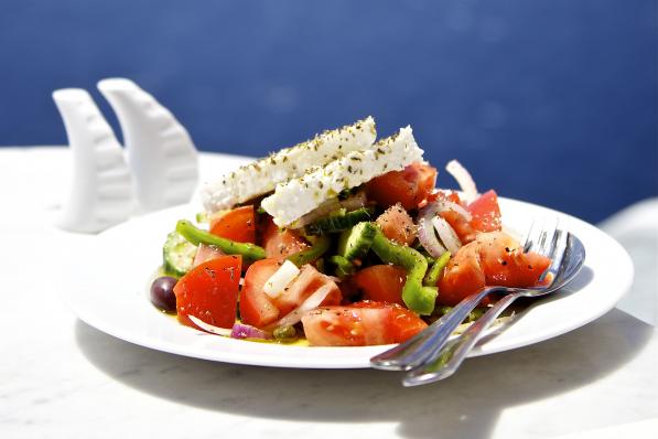 Greek salad on white plate in front of sea.