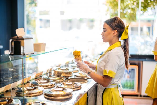 Young woman serving a scoop of ice cream in an ice cream cone in an ice cream shop.