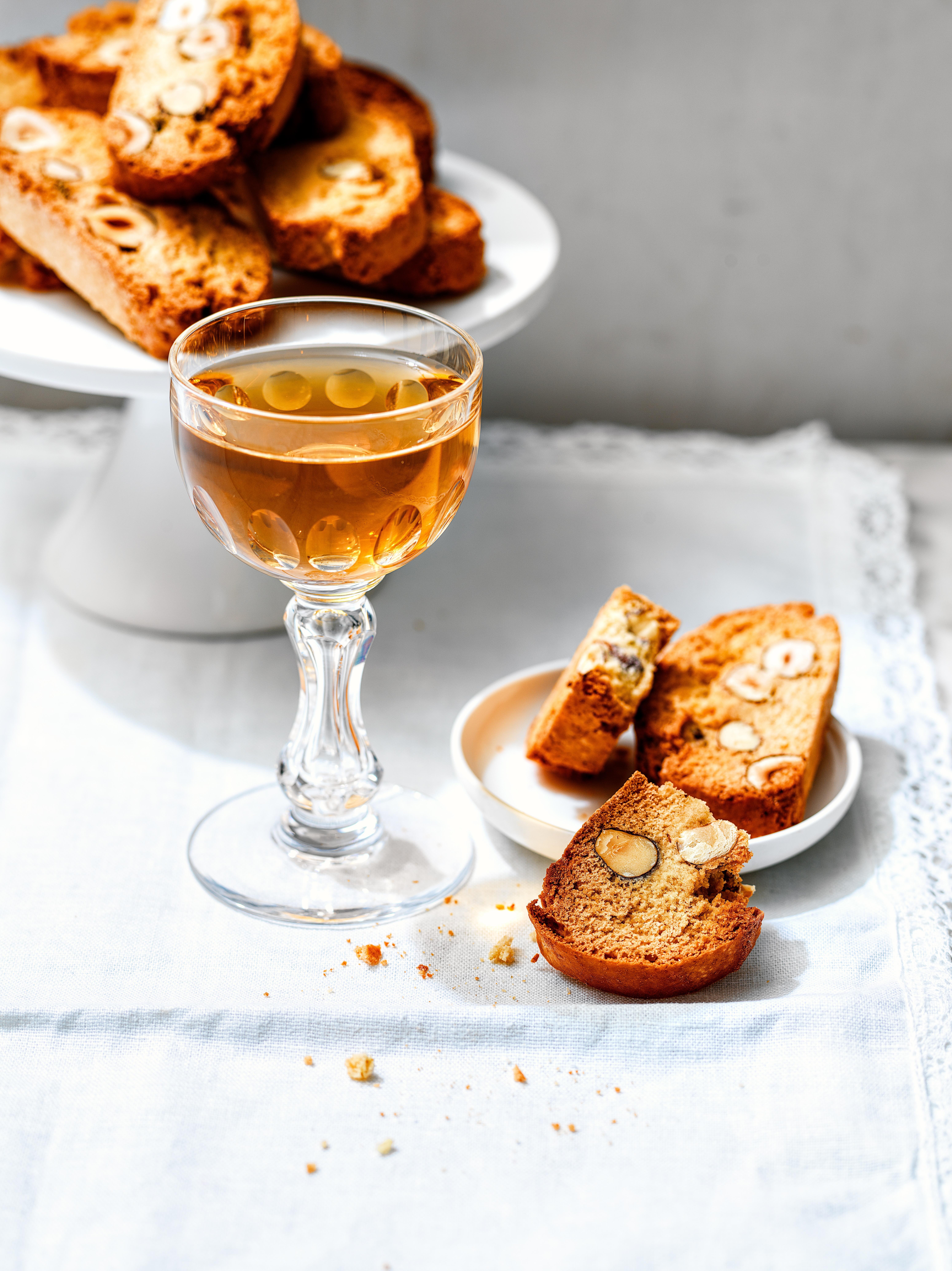 Welke Italiaanse wijn drink je bij het dessert: een glas vinsanto met Cantuccini-koekjes op een wit tafelkleed.