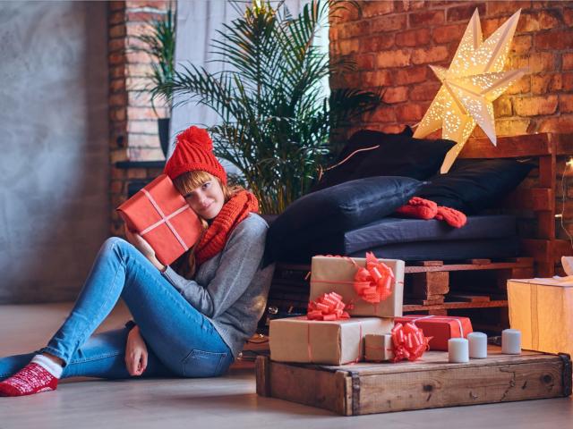 femme assise enlaçant un cadeau de Noël, entourée de paquets sous le sapin